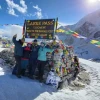 Group of trekkers posing at the Larke Pass (5106m) sign on the Manaslu Circuit Trek surrounded by snow-covered mountains and colorful prayer flags.