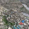 Aerial view of Narphu village in the remote Nar Phu Valley, showing stone-built houses clustered on a rugged hillside beside terraced fields and a river gorge in the Himalayas.